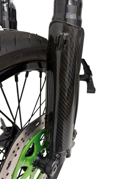 A close up picture of the carbon fiber fork guard installed on the bike. White background. The glossy weave pattern is clearly visible.